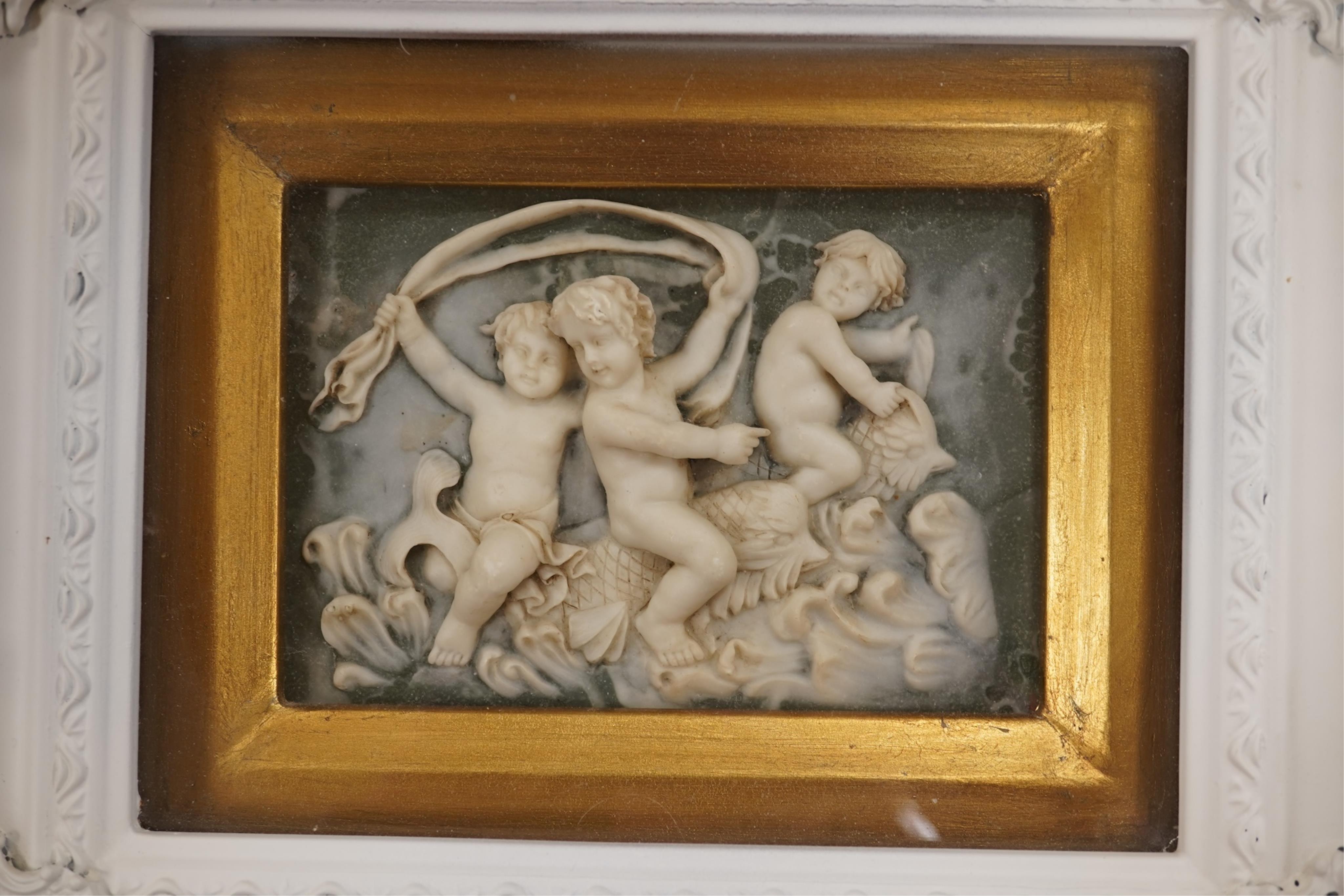 A pair of modern framed carved wax plaques of putti, housed in decorative painted frames, 27 x 32cm